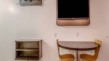 A room with a flat-screen TV mounted on the wall, a small wooden table with two chairs, and a metal shelf unit.