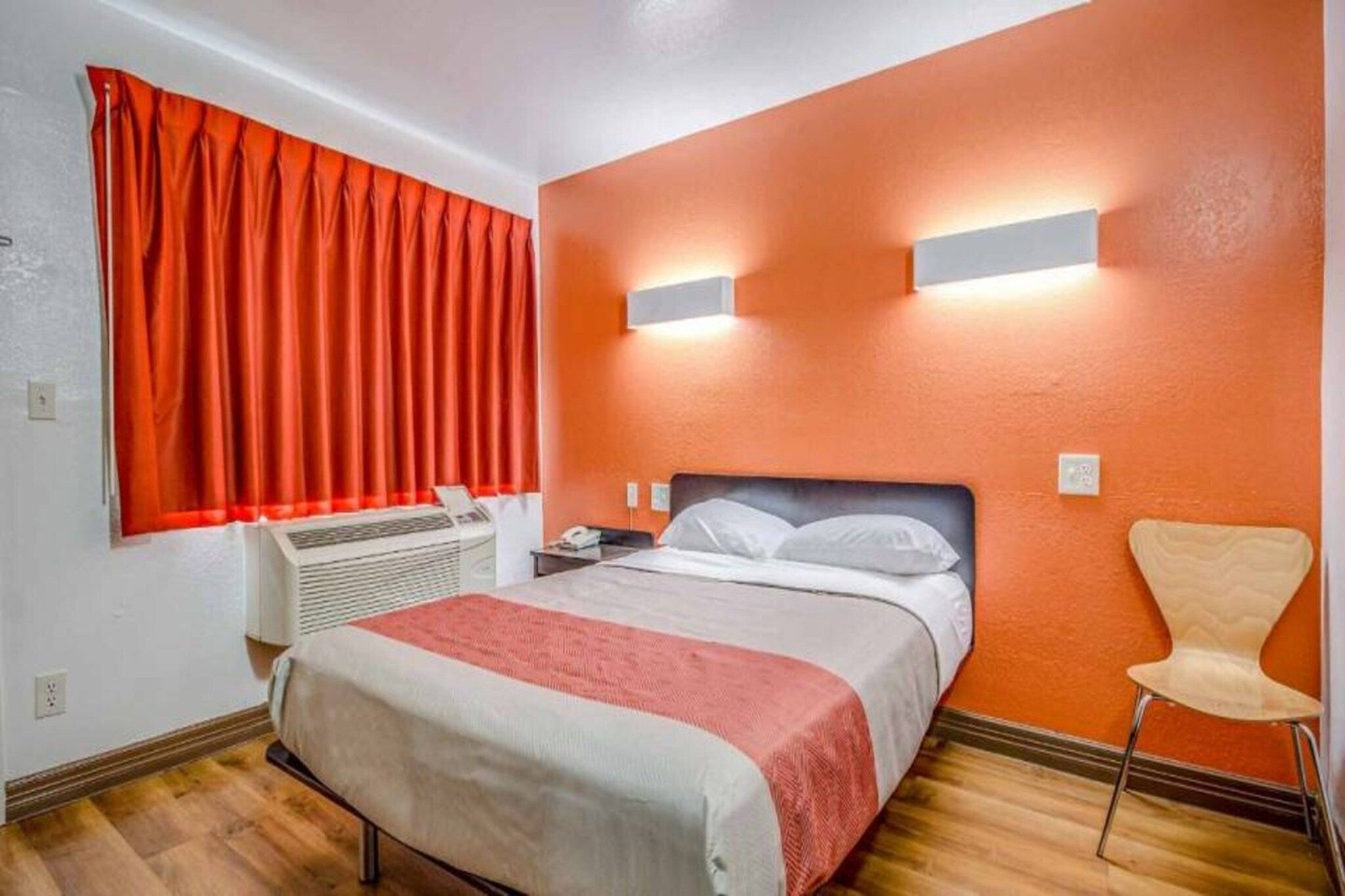 A hotel room with a bed, a chair, a heater, and a window with red curtains.