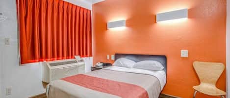 Une chambre d’hôtel avec un lit, une chaise, un radiateur et une fenêtre avec des rideaux rouges.