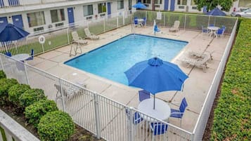 A rectangular pool with a surrounding fence, lounge chairs, and umbrellas.