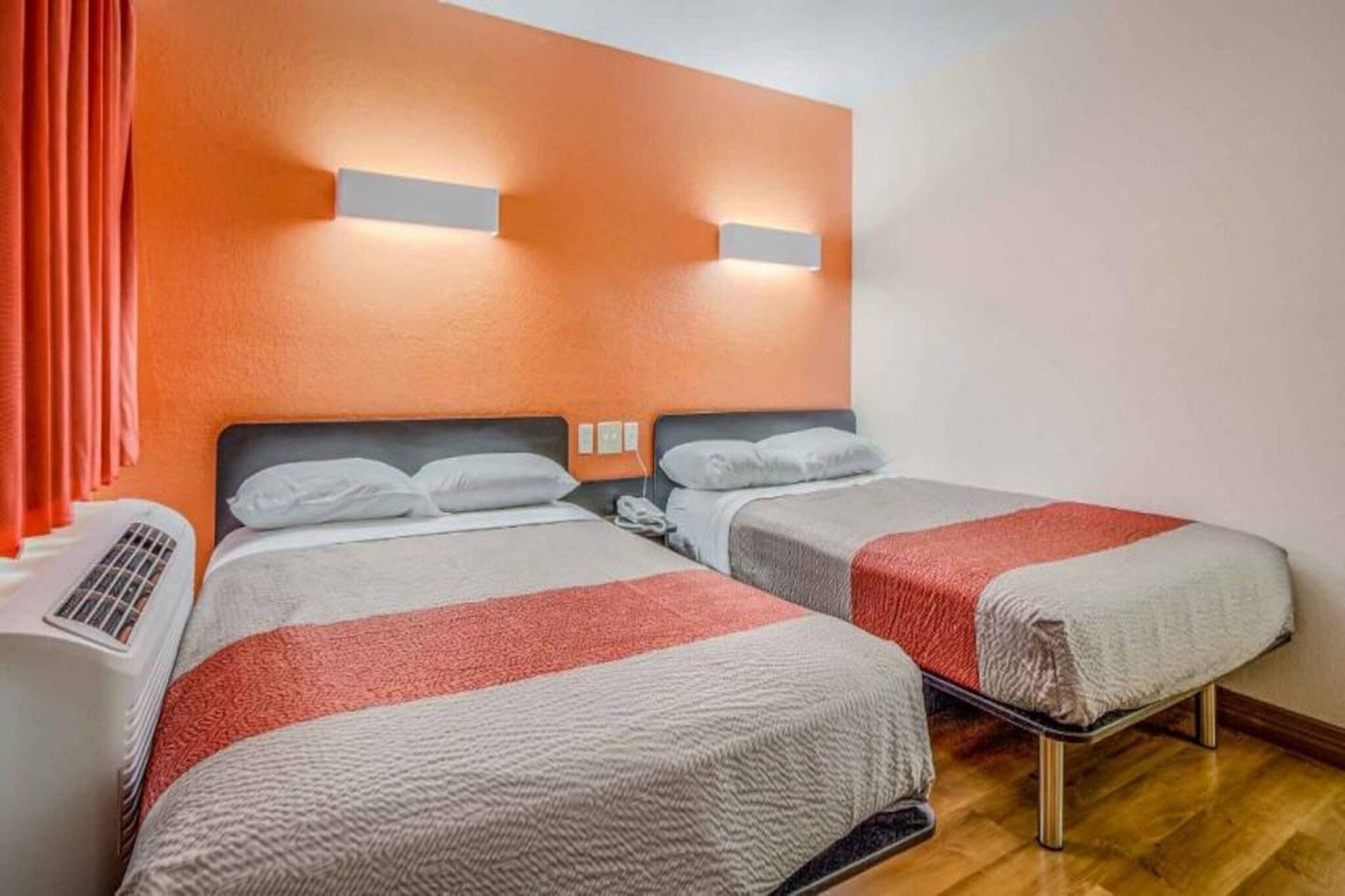 A hotel room with two beds, a heater, and a window with curtains.