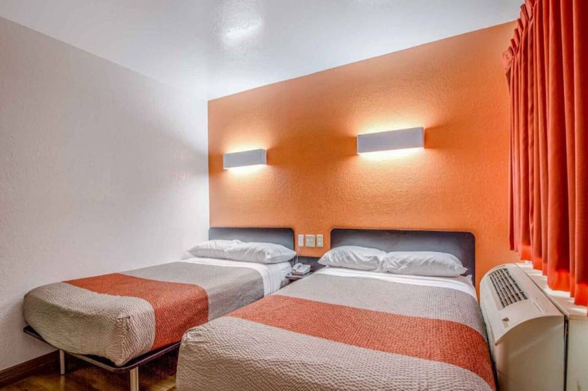 A hotel room with two beds, a wall-mounted air conditioner, and a red curtain.
