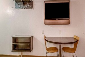 Een kamer met een flatscreen televisie aan de muur, een klein plankensysteem en een tafel met twee stoelen.