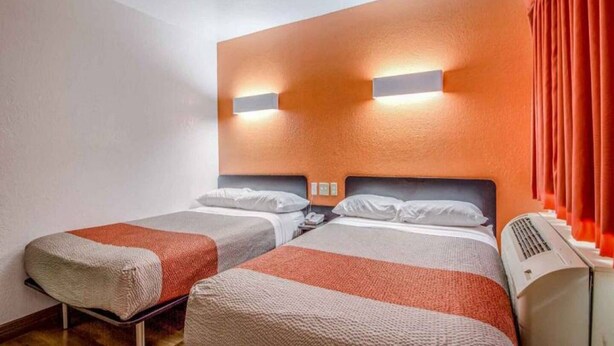 Een hotelkamer met twee bedden, een wandairco en een rood gordijn.