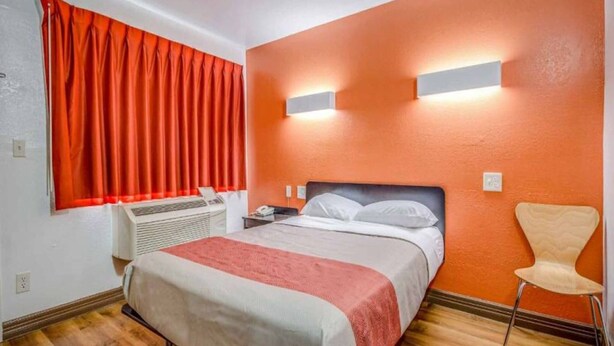 Habitación de hotel con cama, una silla, un calefactor y una ventana con cortinas.