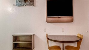 Una habitación con un televisor montado en la pared, una pequeña estantería y una mesa con dos sillas.