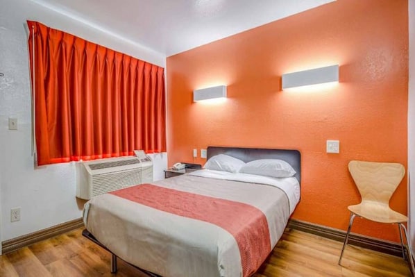 Ein Hotelzimmer mit einem Bett, einem Sessel, einem Heizgerät und einem Fenster mit Vorhängen.