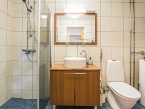 Un baño con cabina de ducha de vidrio, tocador de madera con lavamanos y espejo, y un inodoro.
