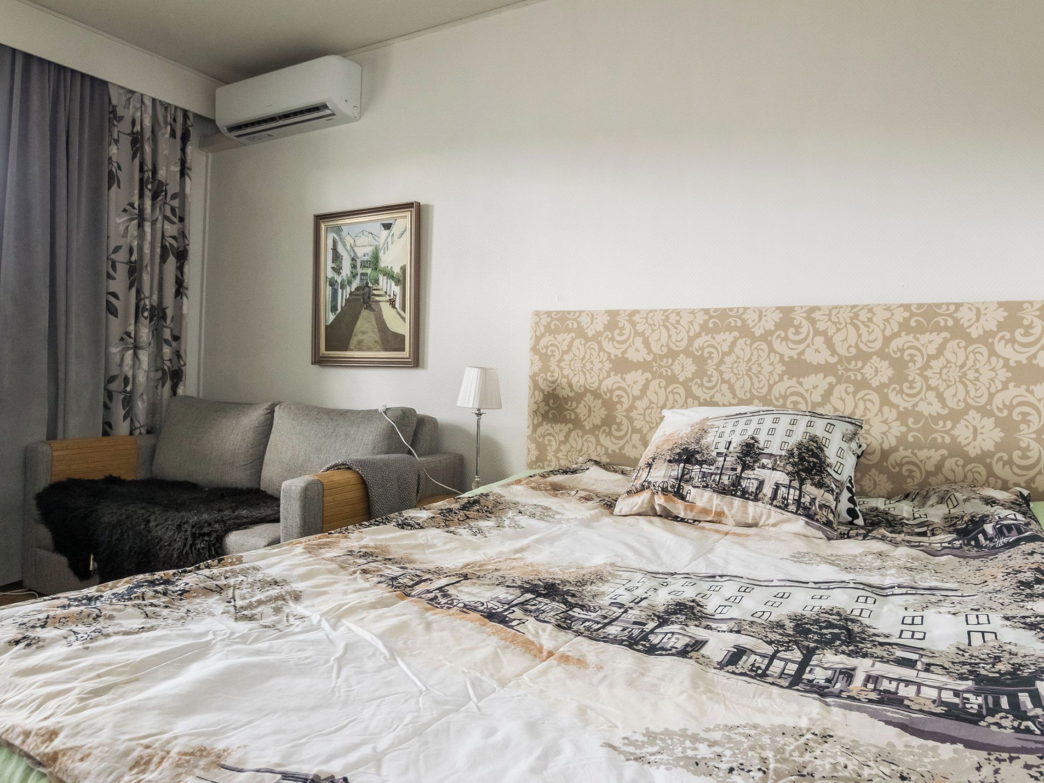 Quarto de hotel com uma cama, uma cadeira, um abajur e um quadro na parede.