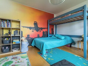 A room with a bunk bed, a bookshelf, a cityscape mural, and a colorful rug.