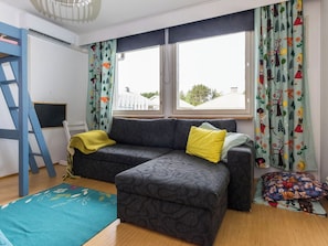 Una habitación con un sofá gris, una manta amarilla, una escalera azul y una alfombra colorida.