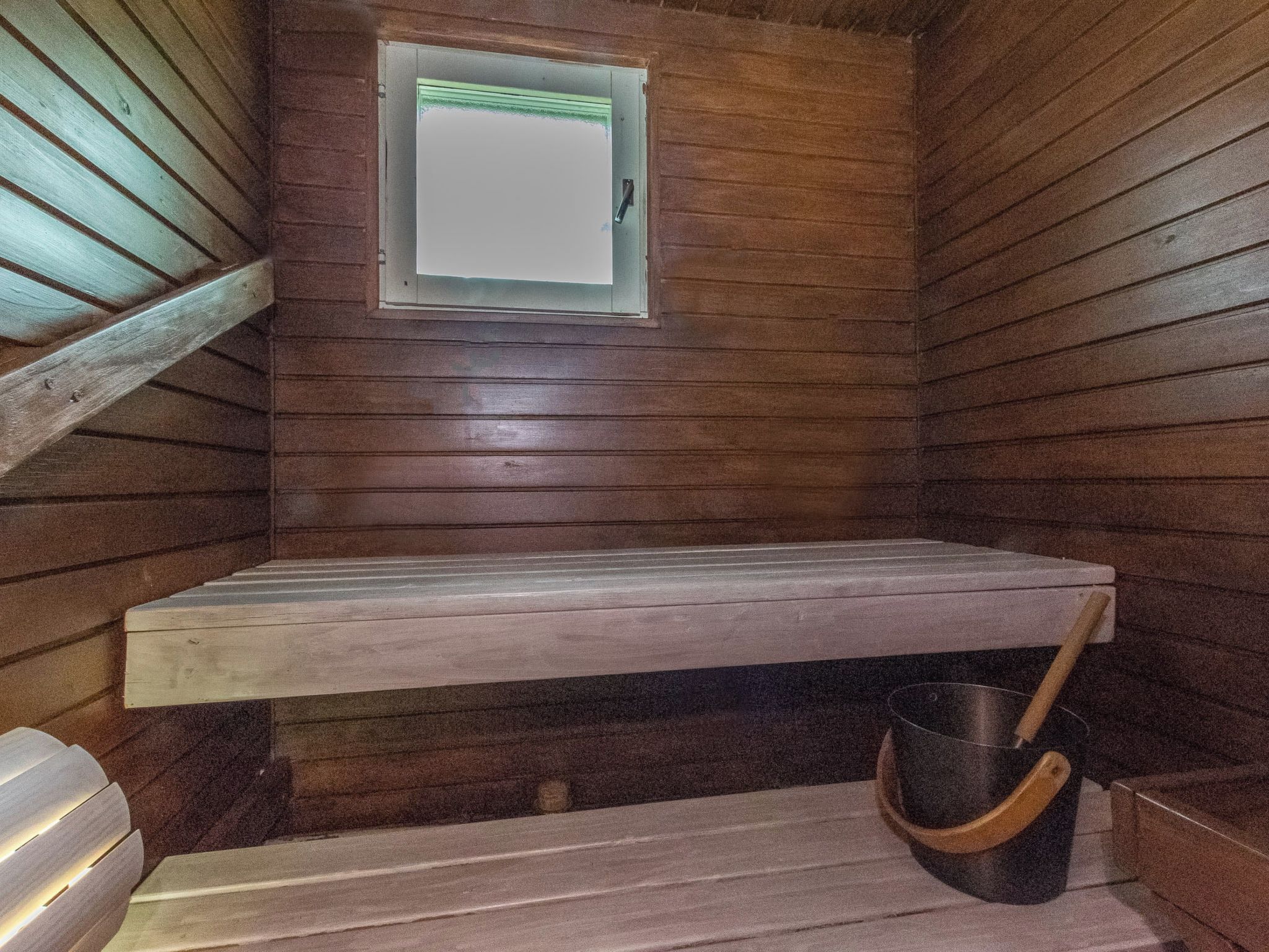 A wooden cabin interior with a bench, a window, and a bucket.