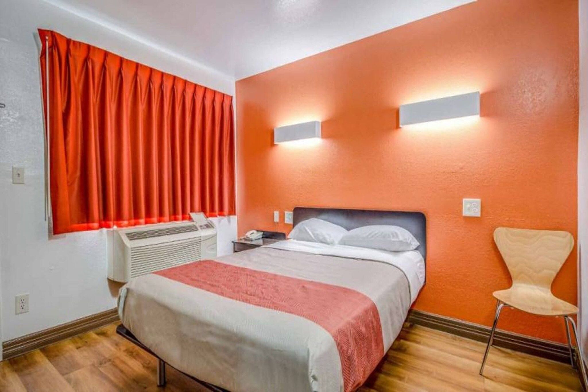 A hotel room with a bed, a chair, a heater, and a window with curtains.