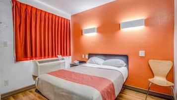 A hotel room with a bed, a chair, a heater, and a window with curtains.