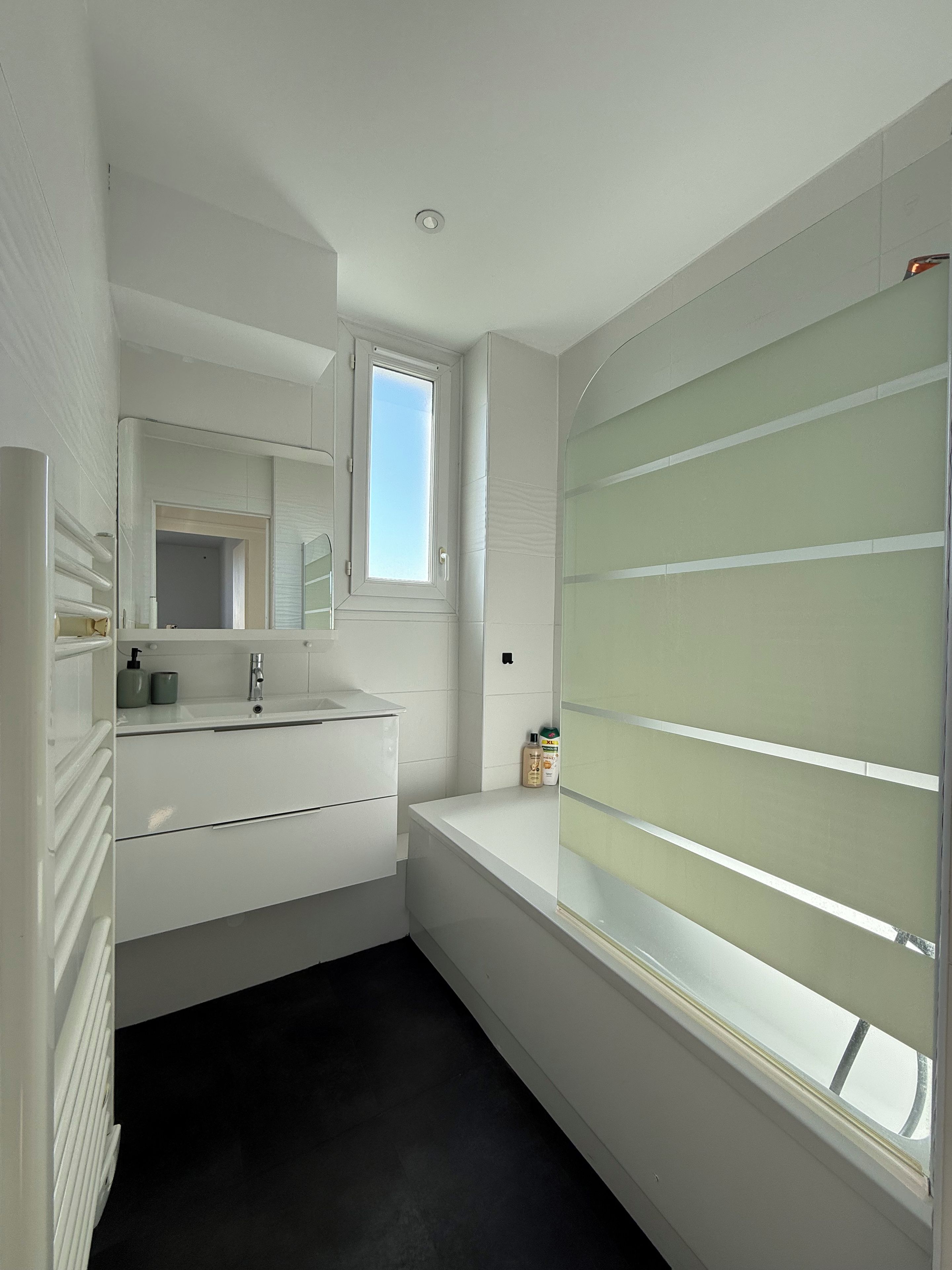 Ein Badezimmer mit weißem Waschtisch, einem Spiegel, einem Fenster und einer Milchglasscheibe.