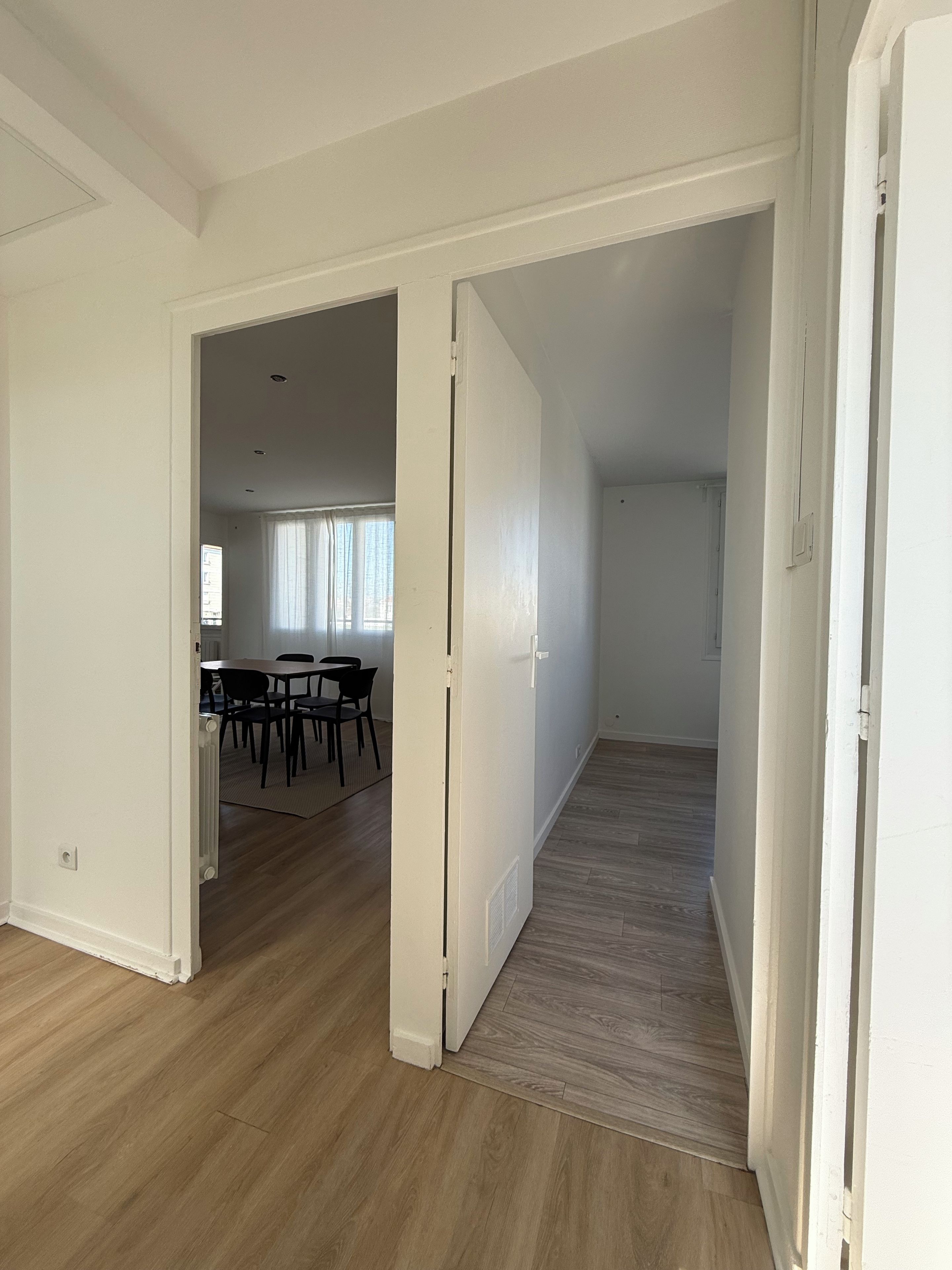 An open-plan living area with a dining table and chairs, a wooden floor, and white walls.