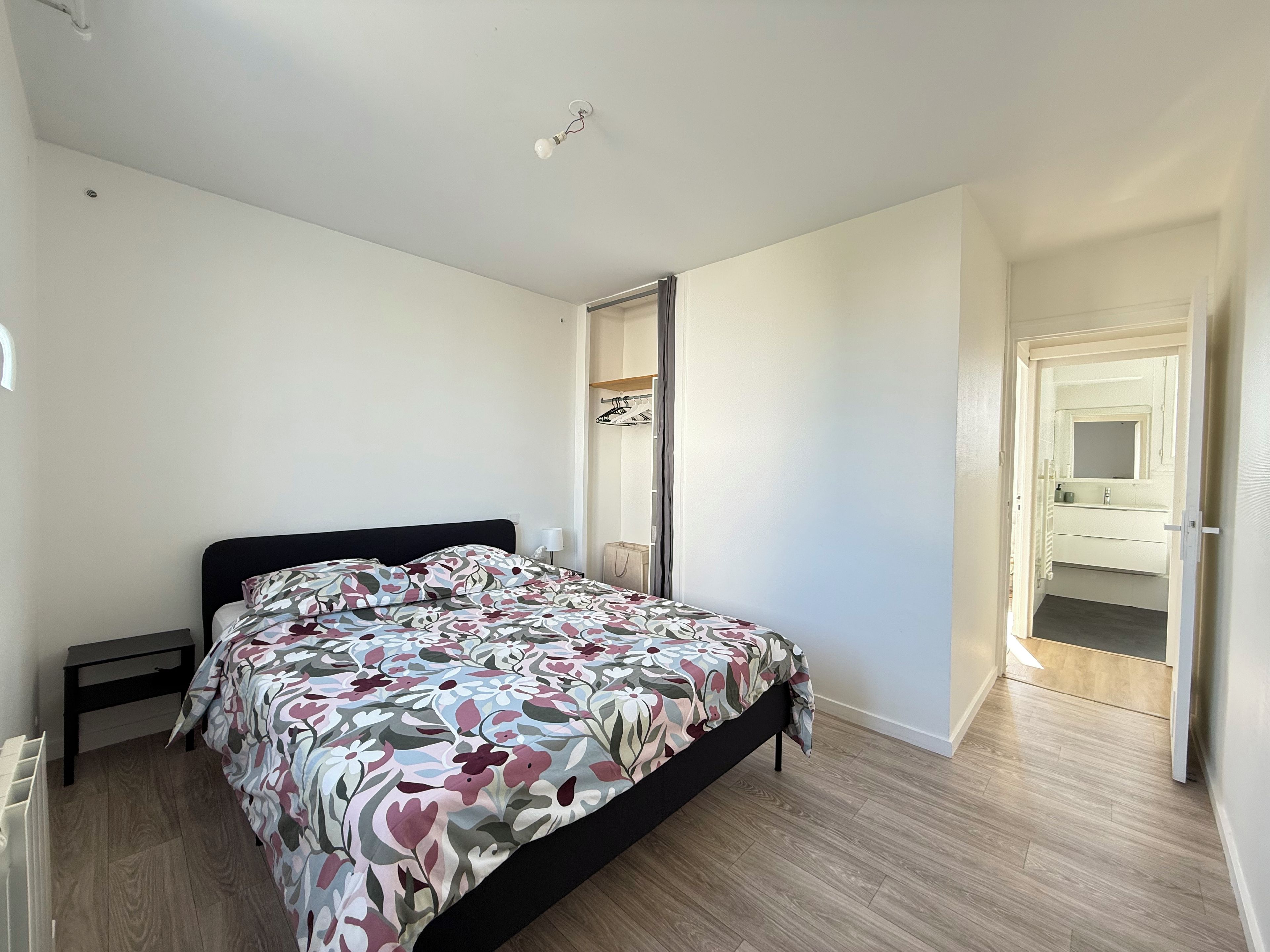 Un dormitorio con cama, mesita de noche, armario y baño visible a través de una puerta abierta.
