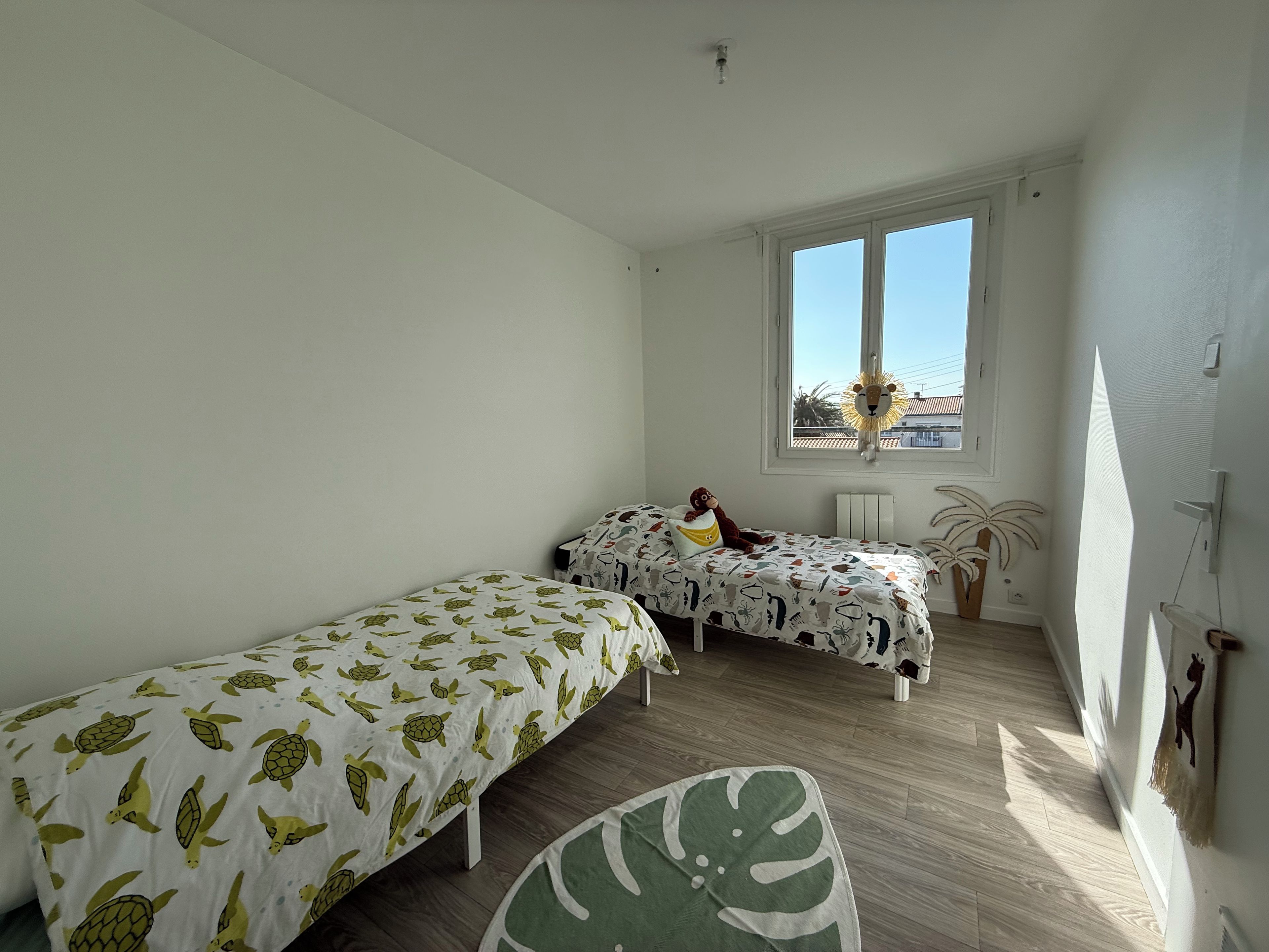 A bedroom with two single beds, a window, a ceiling light, and a wall-mounted radiator.