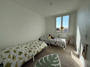 A bedroom with two single beds, a window, a ceiling light, and a wall-mounted radiator. - Spacious & Bright Apartment - Sleeps 6 - Rochefort (Rochefort)