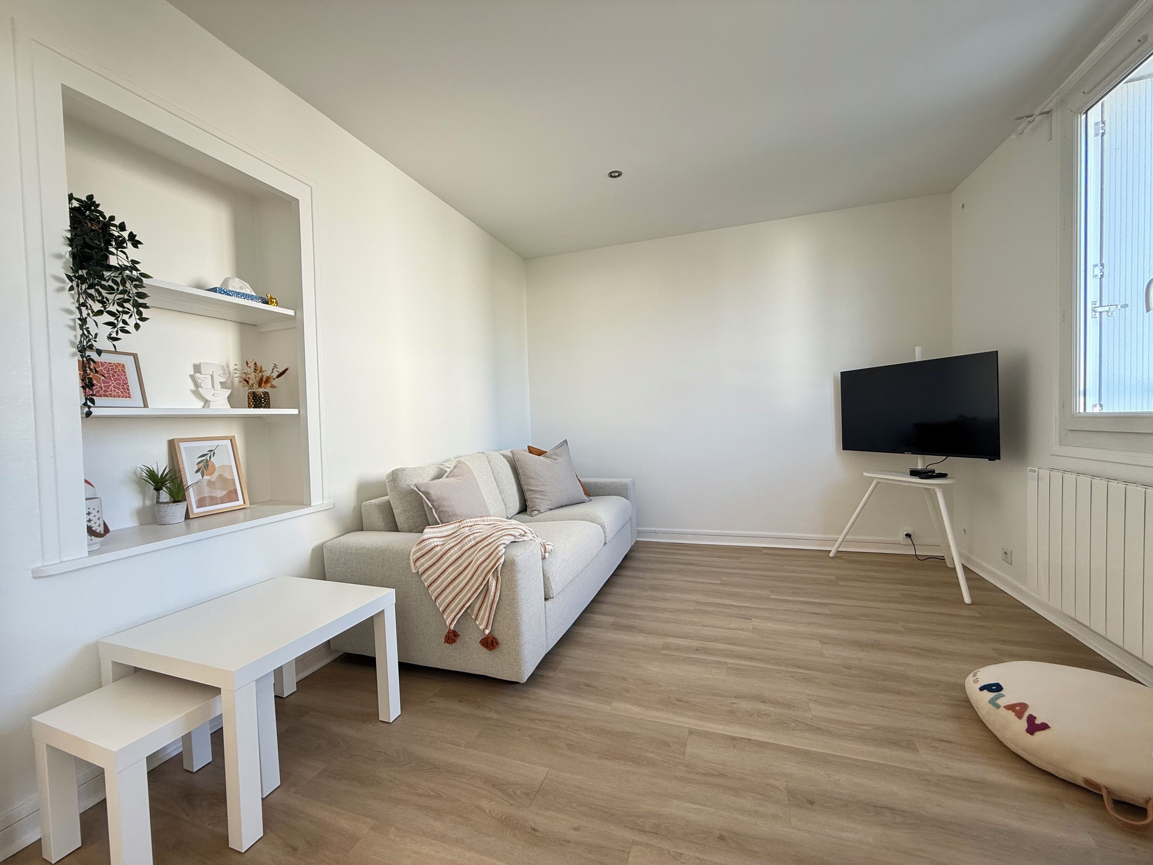 Una sala de estar minimalista con un sofá, un televisor sobre un mueble bajo, una mesa blanca y un banco.