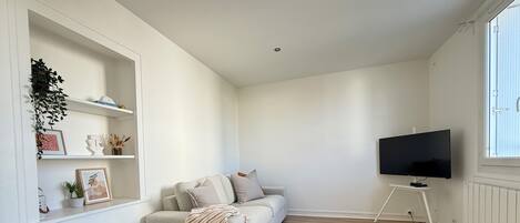 Una sala de estar minimalista con un sofá, un televisor sobre un mueble bajo, una mesa blanca y un banco.