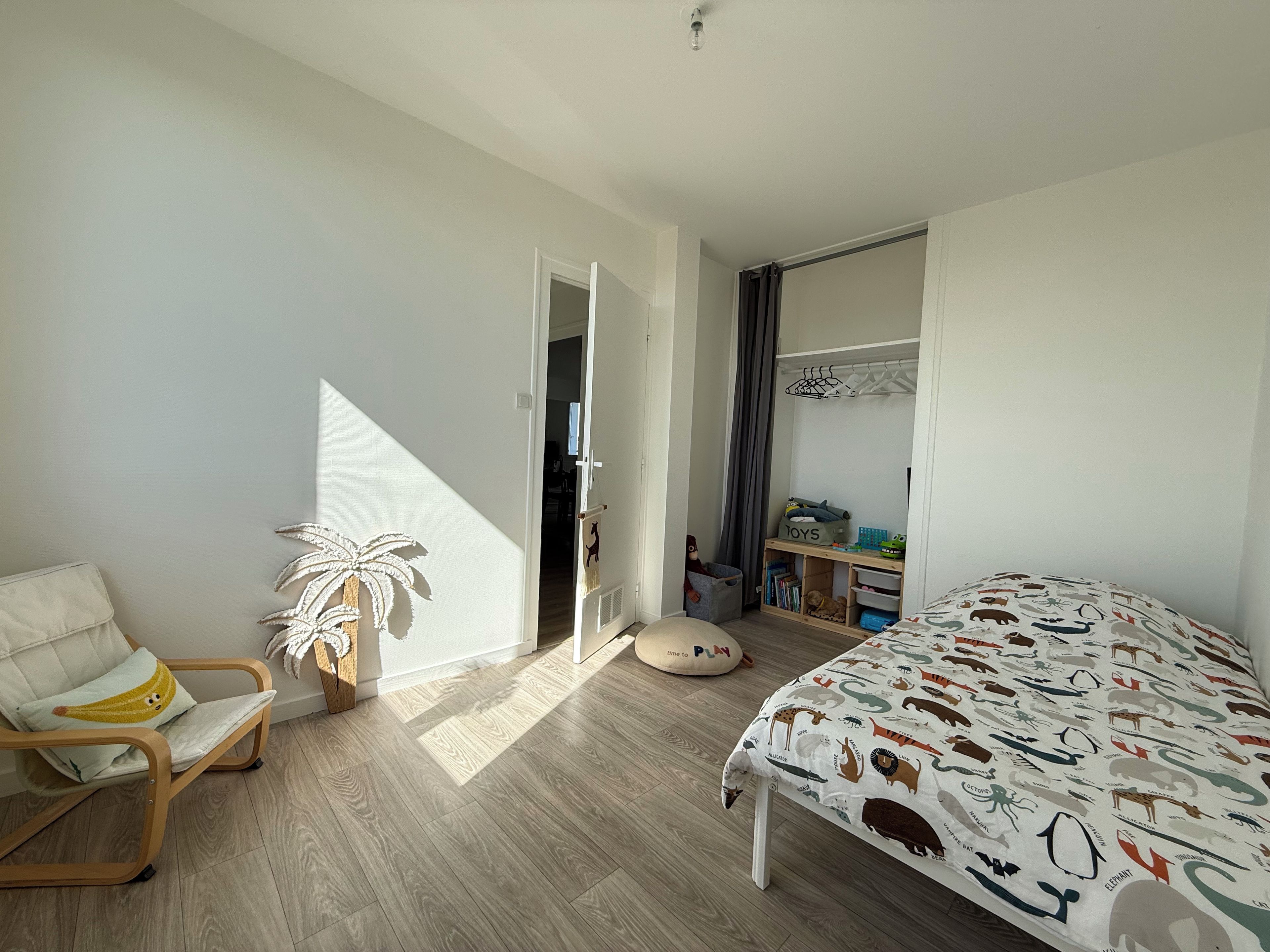 Ein Schlafzimmer mit einem Bett, einem Sessel, einem Kleiderschrank und einer Tür zu einem anderen Raum.