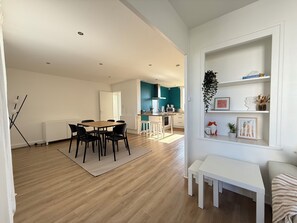A modern living space with a dining area, kitchen, and a white shelving unit with decorative items. - Spacious & Bright Apartment - Sleeps 6 - Rochefort (Rochefort)