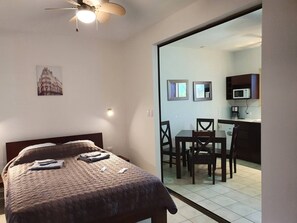 A bedroom with a bed, a ceiling fan, and a view into a dining area with a table and chairs. - Marina Loft unit 103  1 floor (Coco)