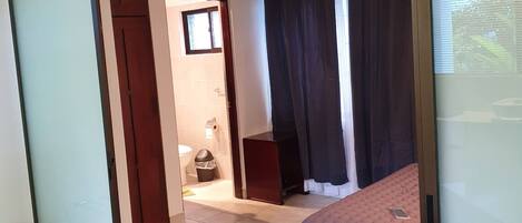 A room with a bed, a chair, a table, a ceiling fan, and a window.