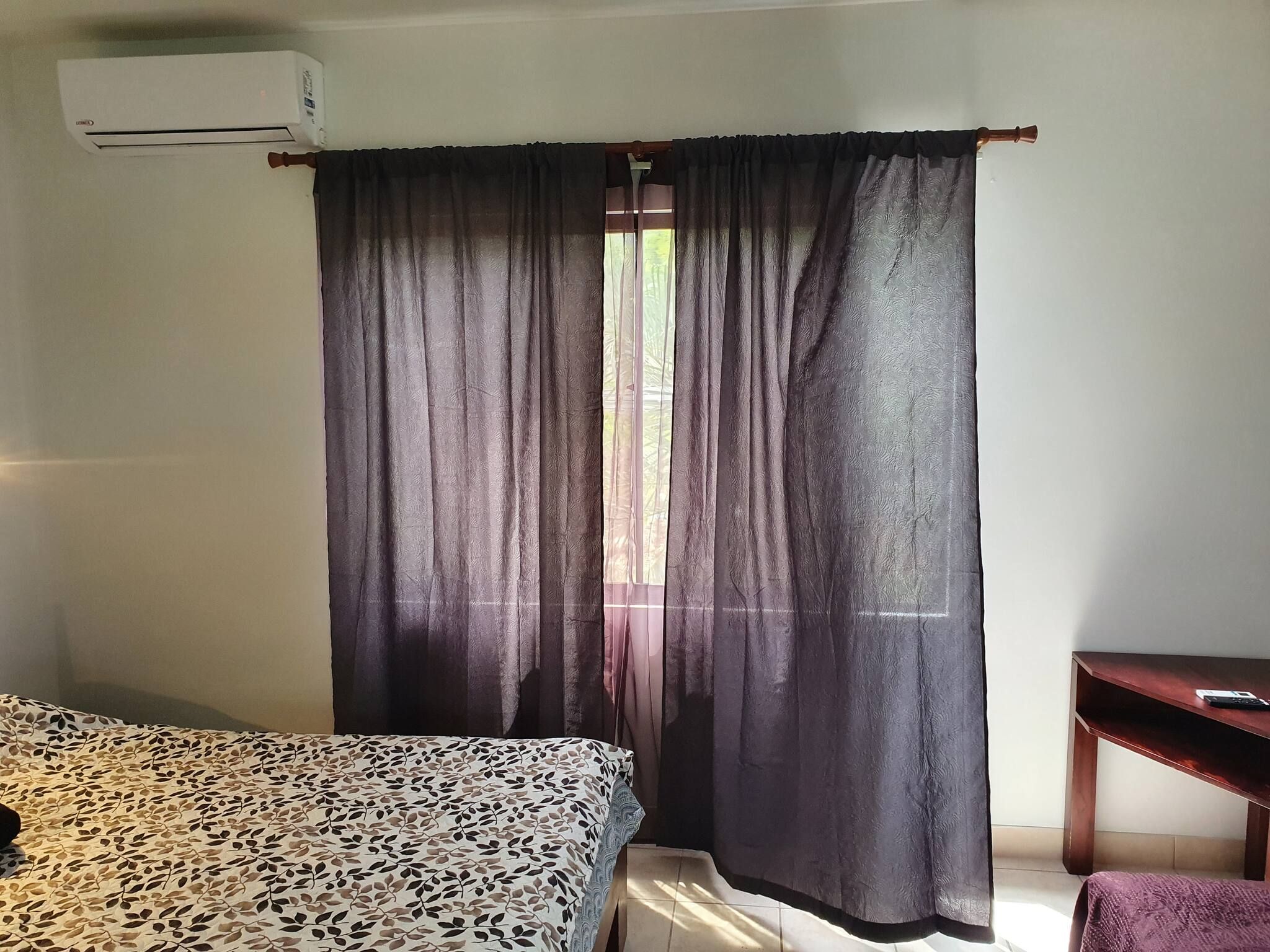 A room with a bed, a desk, and a window with curtains.