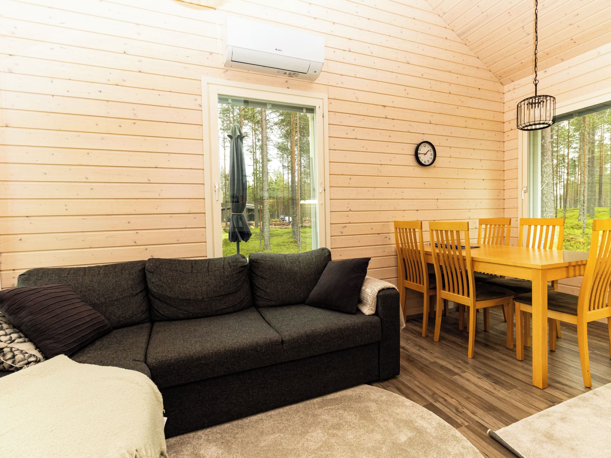L’intérieur d’un chalet accueillant, avec un canapé, une table à manger, des chaises et une horloge au mur.