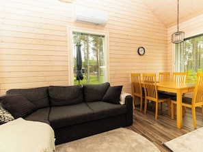 A cozy cabin interior with a sofa, dining table, chairs, and a clock on the wall.