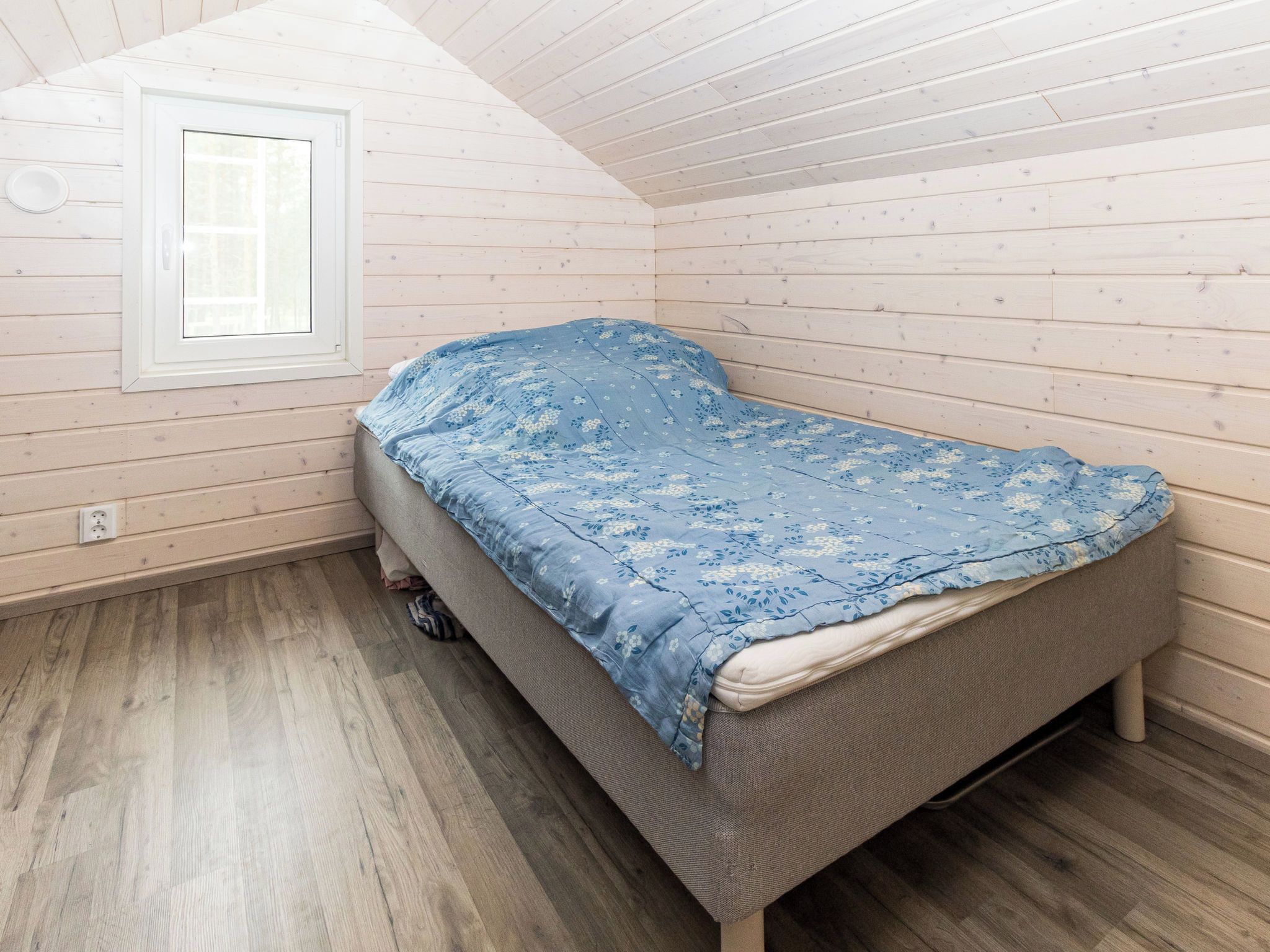 Un lit simple dans une pièce aux murs en bois et au plafond en pente.