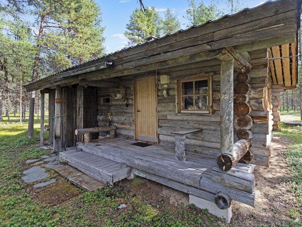 Une cabane rustique en rondins de bois, dotée d’un porche, d’une porte et d’une fenêtre.