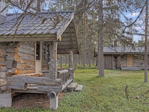 Une cabane rustique en rondins de bois, dotée d’une véranda et entourée d’arbres.