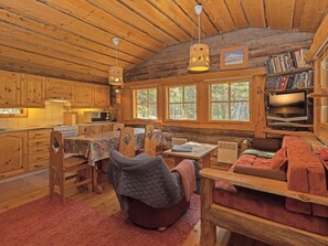 L’intérieur chaleureux d’un chalet avec des murs en bois, un coin repas, un canapé et un téléviseur.