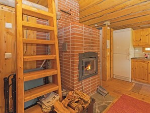 Un intérieur rustique avec une cheminée en briques, des étagères en bois, une échelle et un coin cuisine.