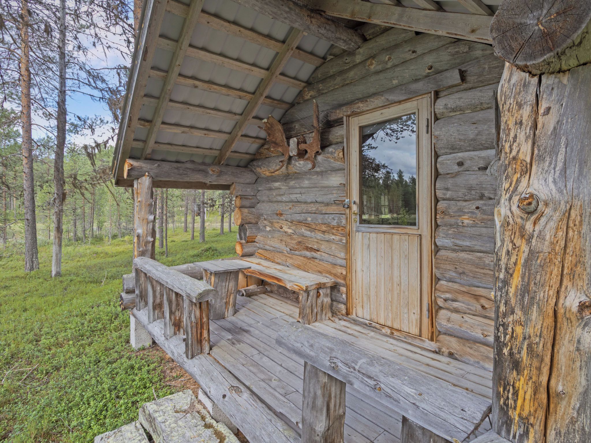 Une cabane rustique en rondins de bois, dotée d’un porche, d’une porte et d’une fenêtre.