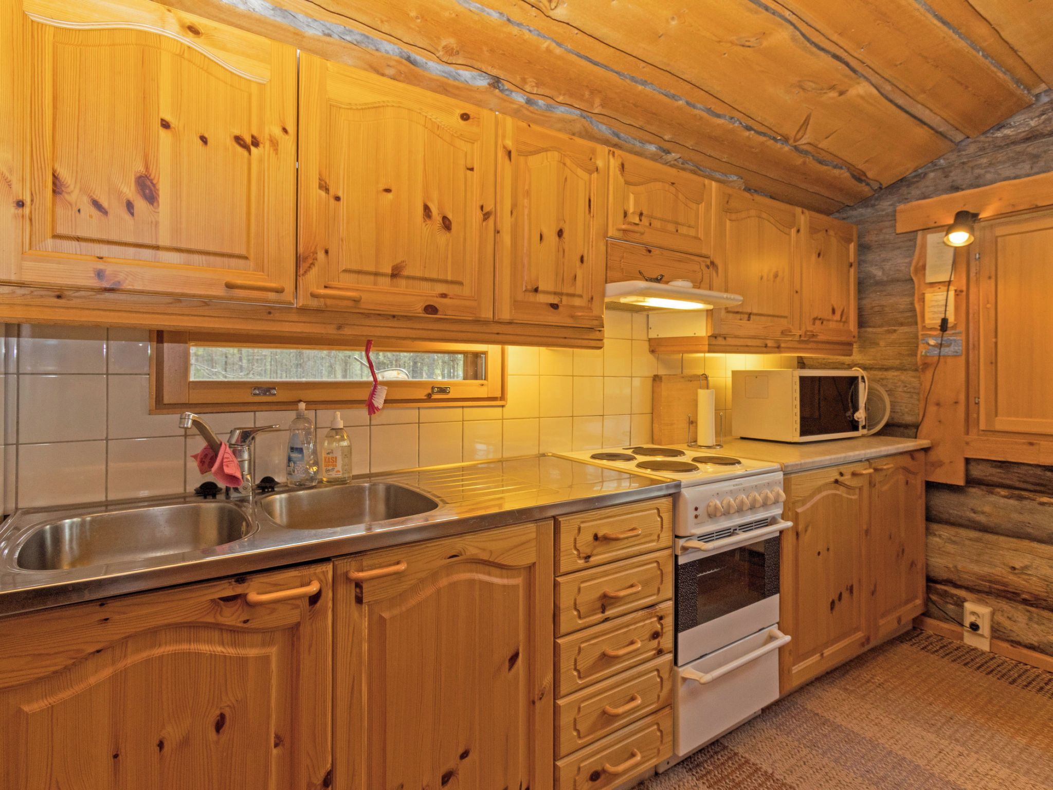 A kitchen with wooden cabinets, a stainless steel sink, a microwave, and a stove.