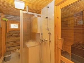 L’intérieur d’un chalet en bois, avec une douche en verre, des murs en bois et une fenêtre.