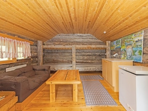 L’intérieur chaleureux d’un chalet avec un plafond en bois, un canapé, une table en bois, un réfrigérateur et des œuvres d’art accrochées aux murs.
