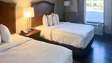 A hotel room with two beds, a nightstand with a lamp, and a view of the outside.