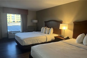 A hotel room with two beds, a nightstand, a lamp, and a view of a building outside. - Comfy 2 Queen Bed|Fridge|Free Wifi (Stafford)