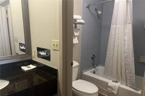 Un baño con encimera negra, lavabo blanco y retrete blanco. Cuenta con ducha con cortina blanca y bañera.