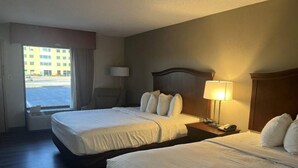 Ein Hotelzimmer mit zwei Betten, einem Nachttisch, einer Lampe und Blick auf ein Gebäude.