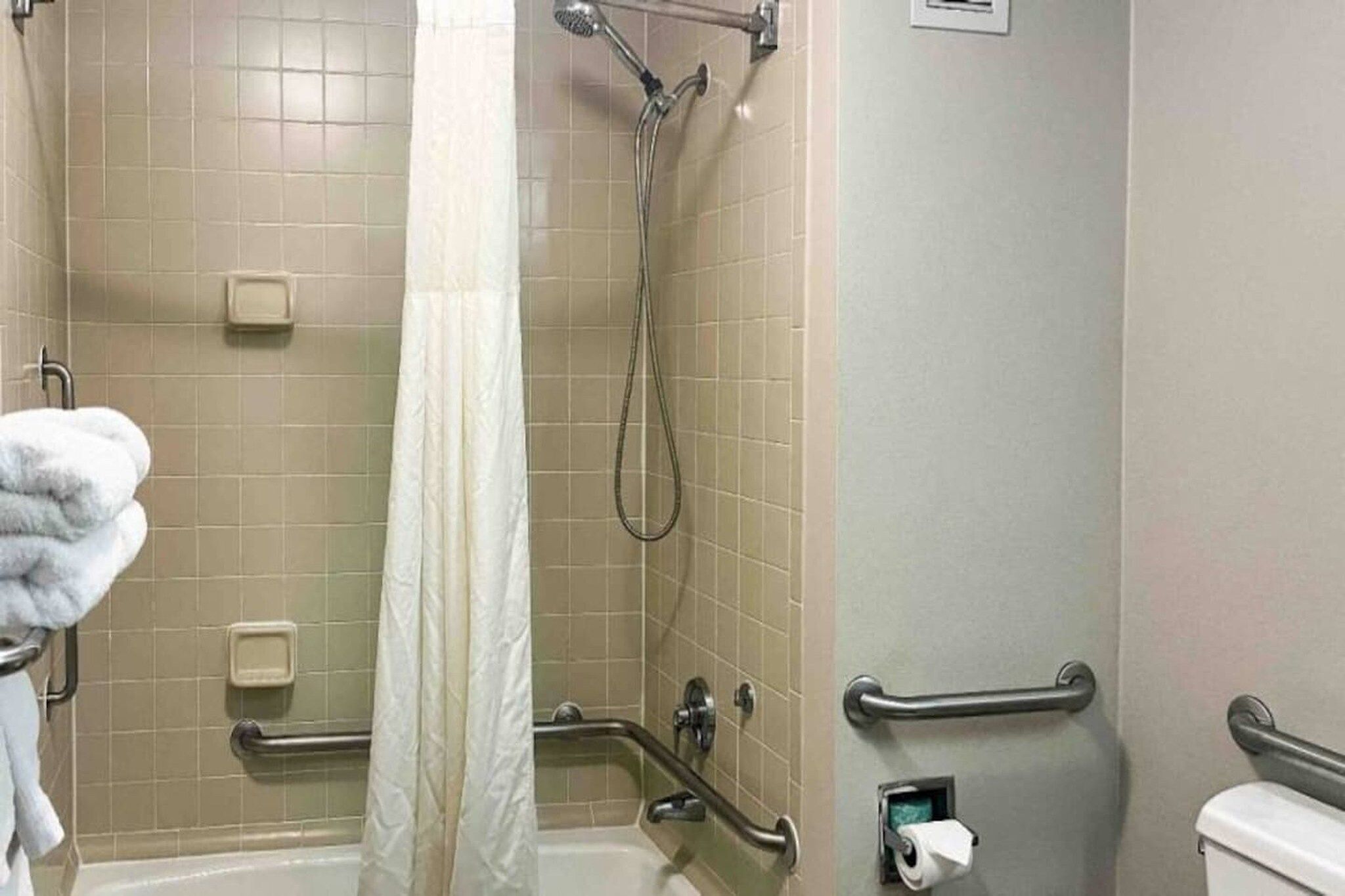 Une salle de bain équipée d’une douche, de barres d’appui, d’un porte-serviettes et de toilettes.