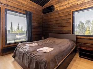 A wooden cabin bedroom with a large bed, two windows with curtains, and a view of trees. - Villa midnight sun by Interhome (Inari)