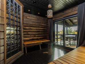A log cabin interior with a bench, a glass door leading outside, and a hanging light fixture. - Villa midnight sun by Interhome (Inari)