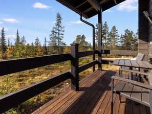 Une terrasse en bois, dotée d’une rambarde, d’une table et de chaises, qui offre une vue sur une zone boisée.