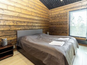 A wooden cabin room with a bed, a nightstand, and a window with blinds. - Villa midnight sun by Interhome (Inari)